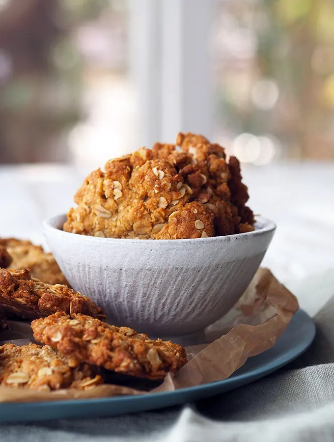 A bowl with freshly baked Anzac biscuits sitting on a plate with more biscuits