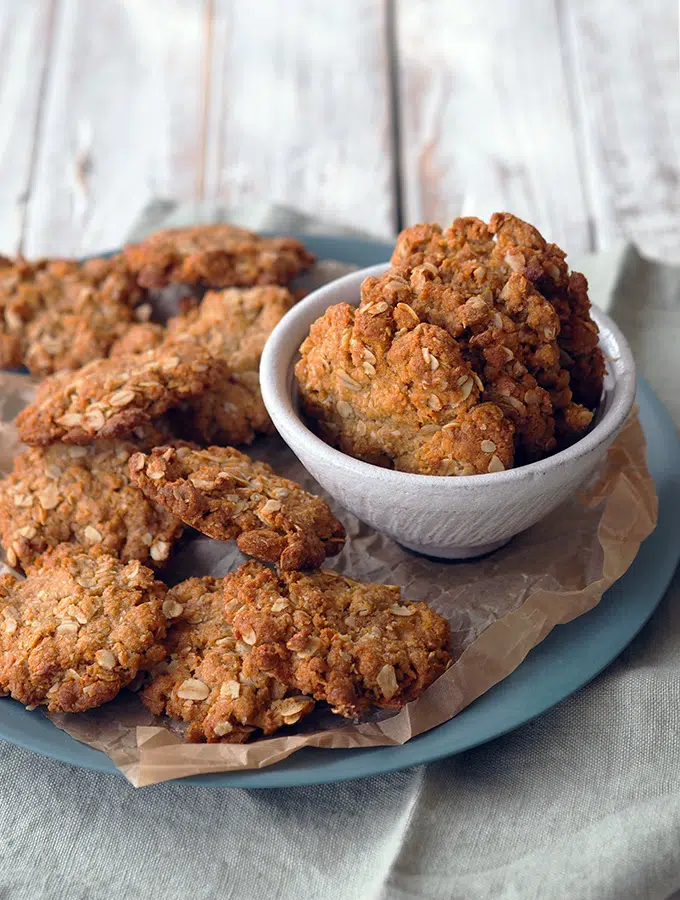 Anzac biscuits in a bowl and on a plate on a wooden table