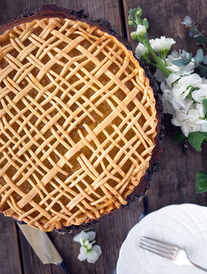 above view of lattice work on the pineapple tart with some white flowers next to the tart, and white plate and fork in bottom right hand corner