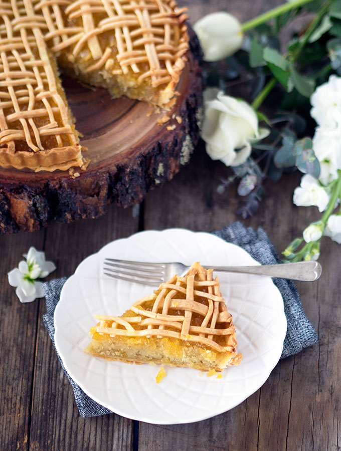 tart on a round wooden board with a slice removed. slice of tart on a white plate in foreground with a fork.