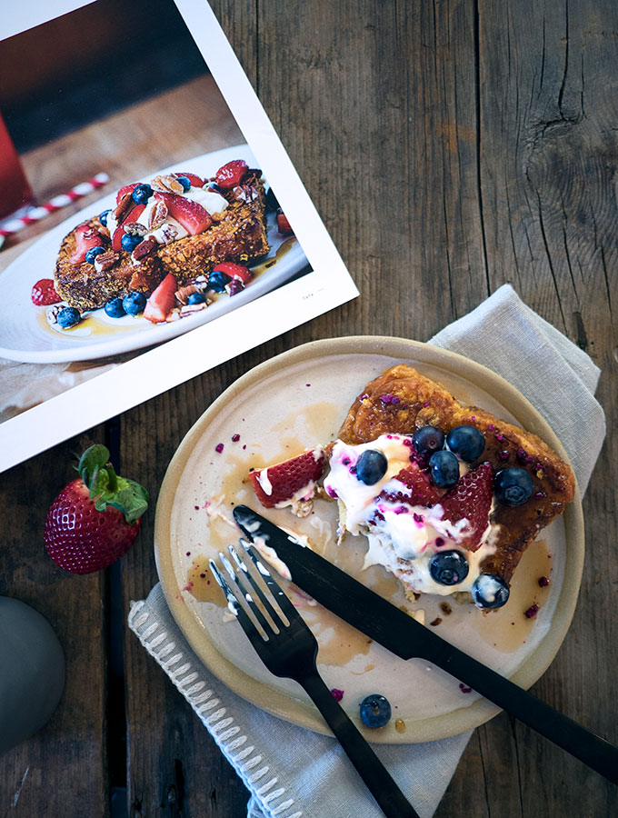 half eaten plate of french toast topped with berries and yoghurt on a stone plate on wooden table