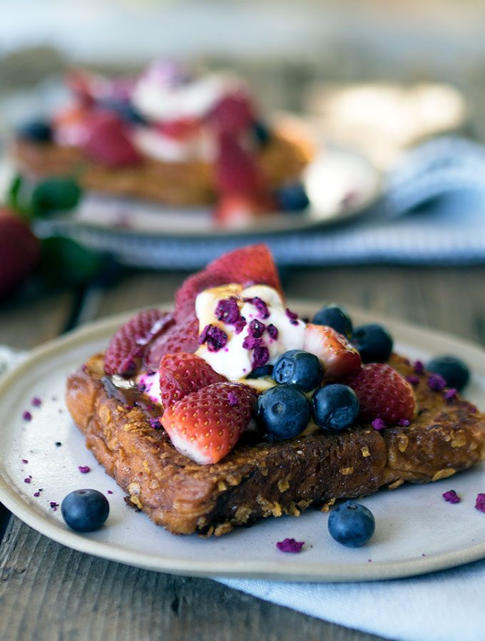 close up photo of cornflake crumbed french toast topped with strawberries and blueberries