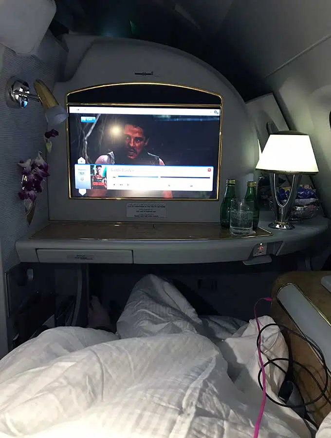 Emirates First Class Sydney to Bangkok passenger lying down in bed of the first class suite watching the entertainment unit