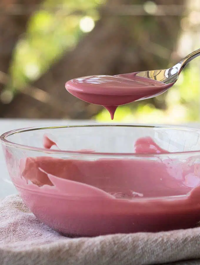 Melted ruby chocolate in a glass bowl dripping from a spoon