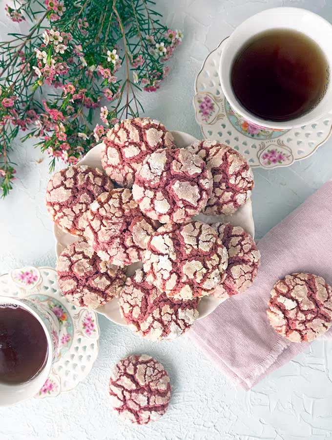 A flat lay view of Ruby Chocolate Crackle Cookies on a plate with tea cups and flowers