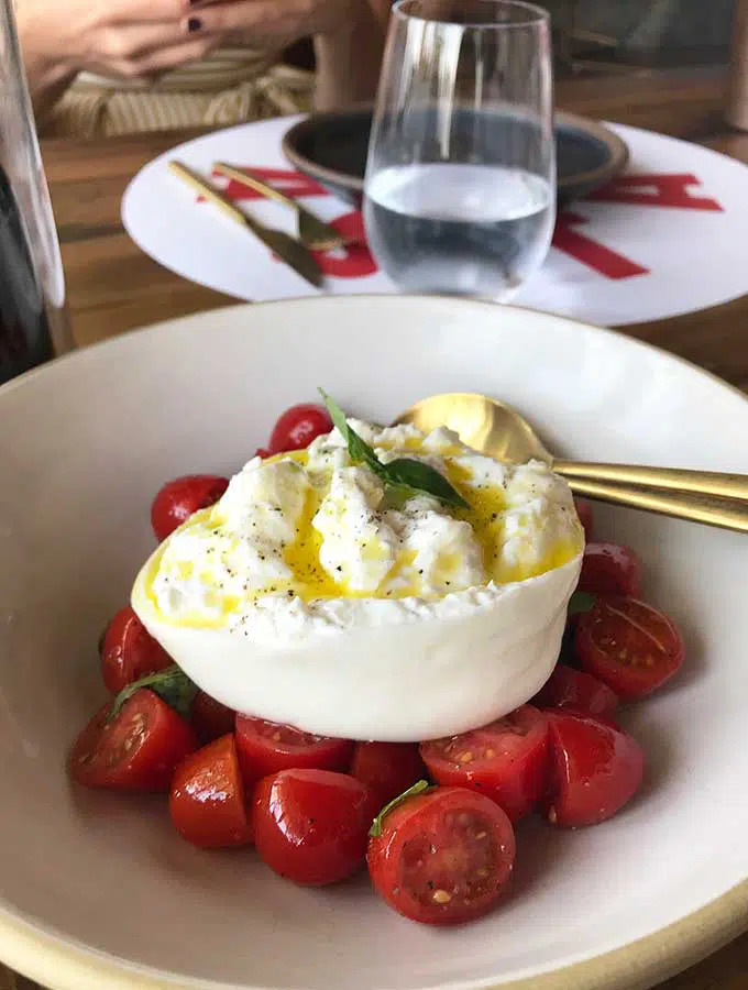 ball of burrata cheese sitting on top of ripe sliced cherry tomatoes in a white bowl