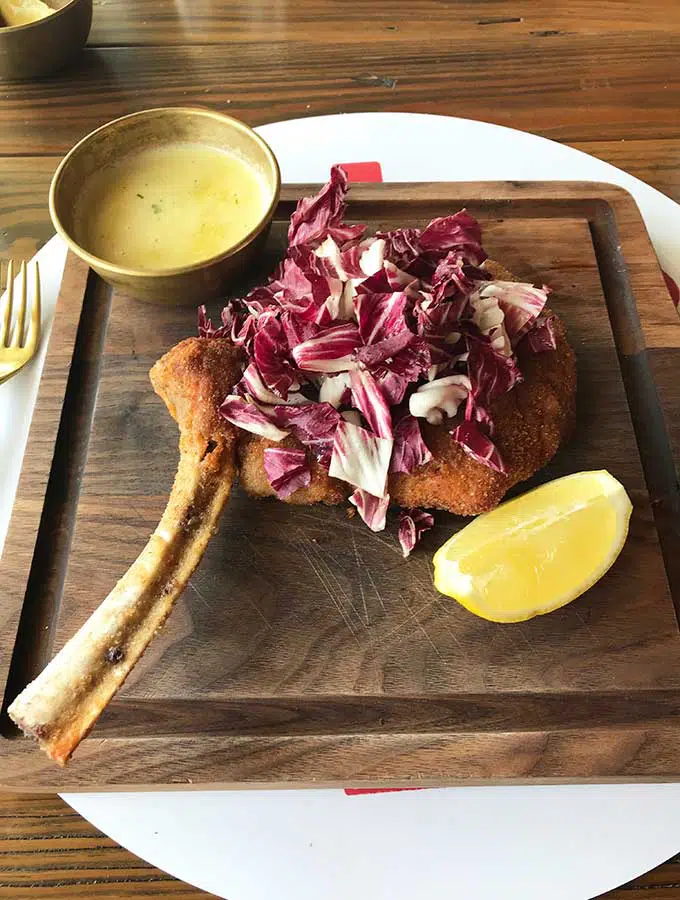 wooden board with fried crumbed veal cutlet, wedge of lemon, dipping sauce and salad