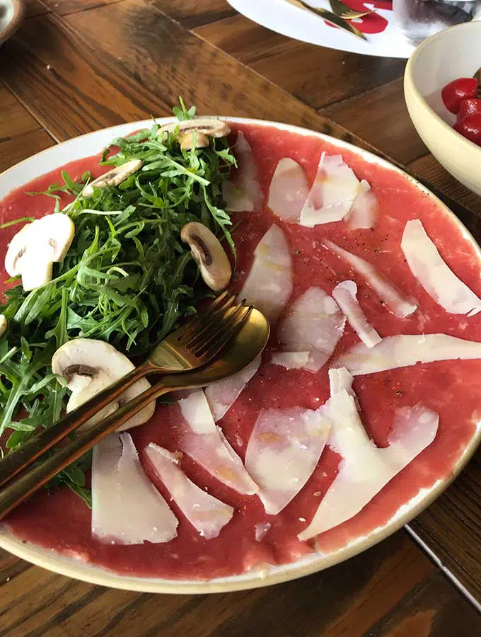 plate with shaved beef topped with shaved parmesan and rocket