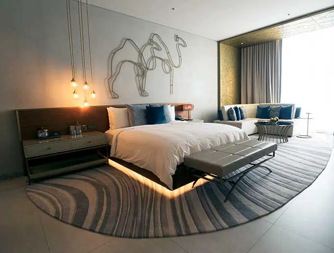 king size bed with rug underneath it. Wire sculpture of camels on the wall above the bed