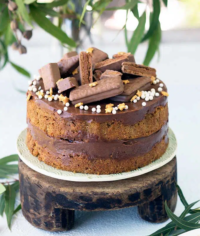 coffee sponge filled with tim tam spread on a wooden cake stand decorated with tim tams