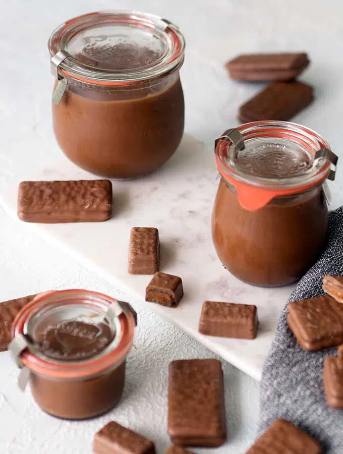 Three glass weck jars with lids containing Tim Tam spread on a marble board with Tim Tams scattered around