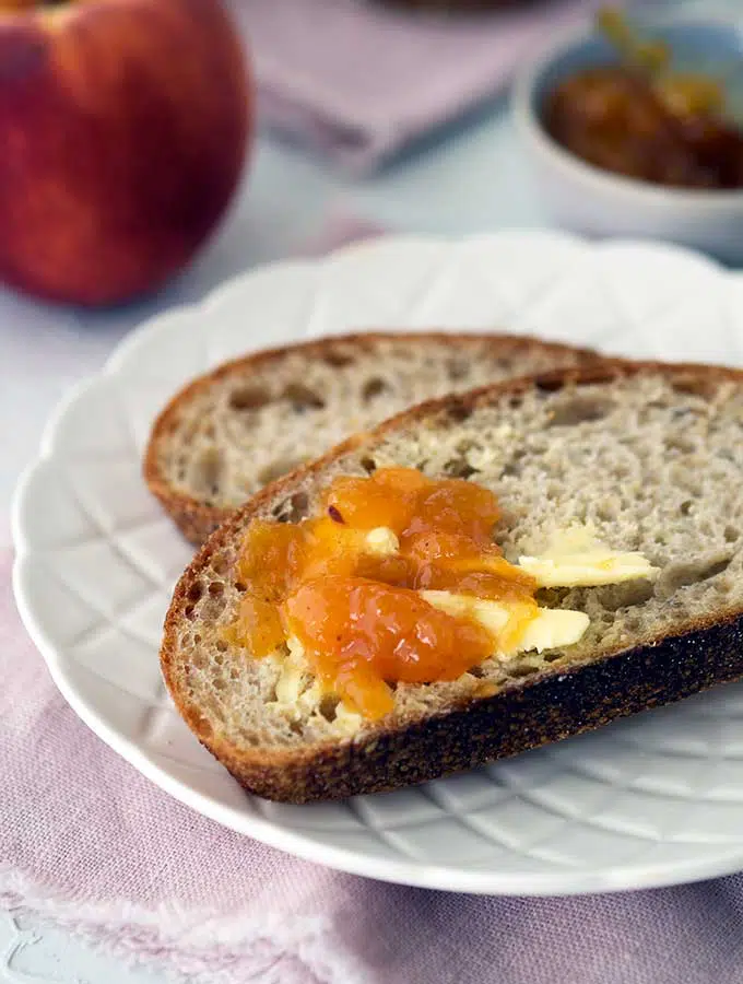 slice of sourdough with butter and peach jam on a plate