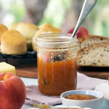 jar of peach bourbon jam with out the lid with a spoon inserted