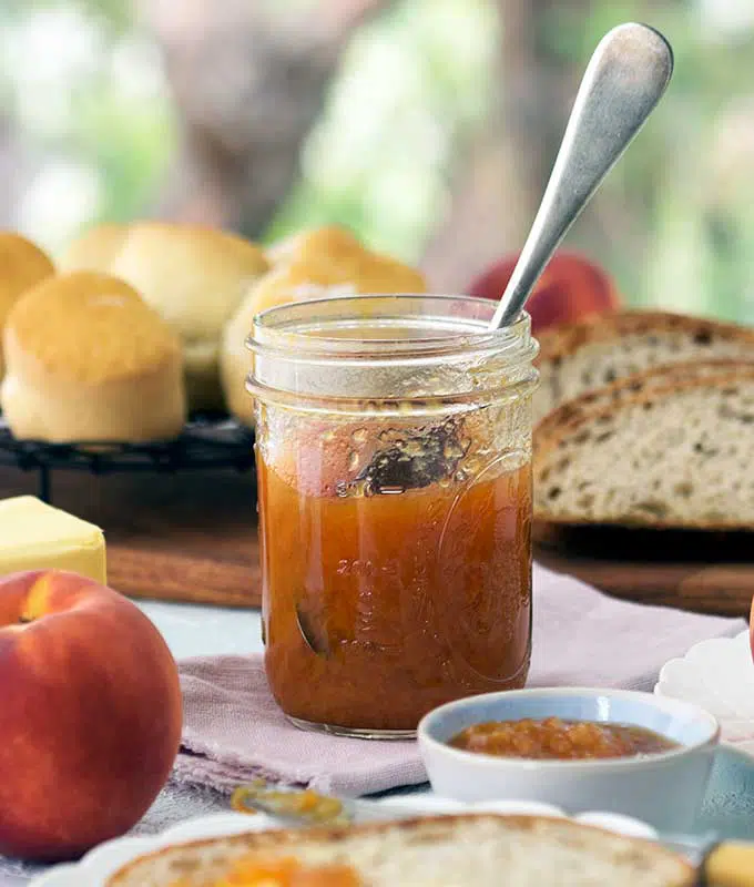 jar of peach bourbon jam with out the lid with a spoon inserted