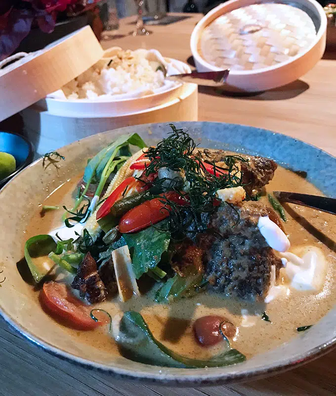 beef cheek curry in a blue bowl with rice in a basket behind
