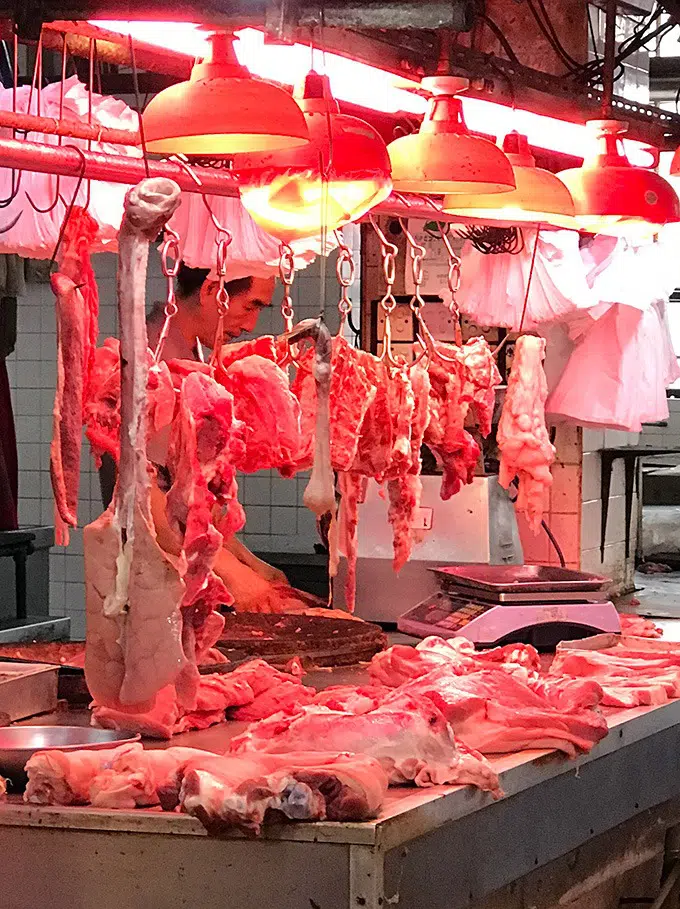 various cuts of meat hang aroudn the butcher at the red market macao