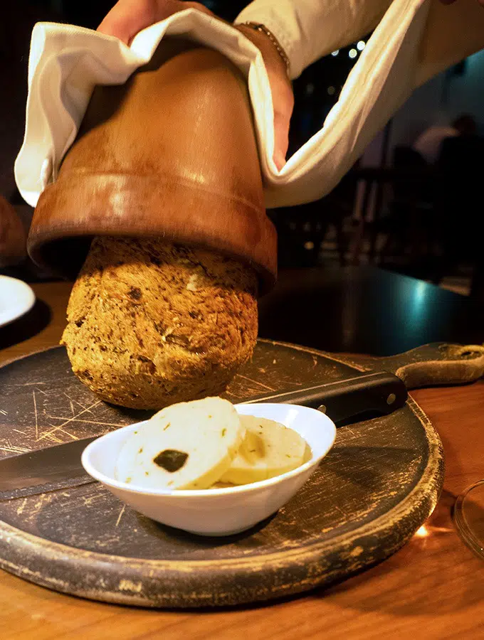 bread being released from the pot it was baked in on to a bread board with butter in a small dish and a knife