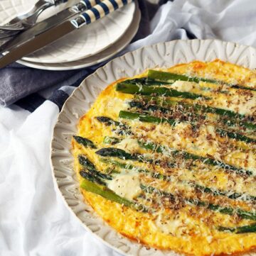above view of asparagus frittata on a white serving plate with smaller serving plates and cutlery