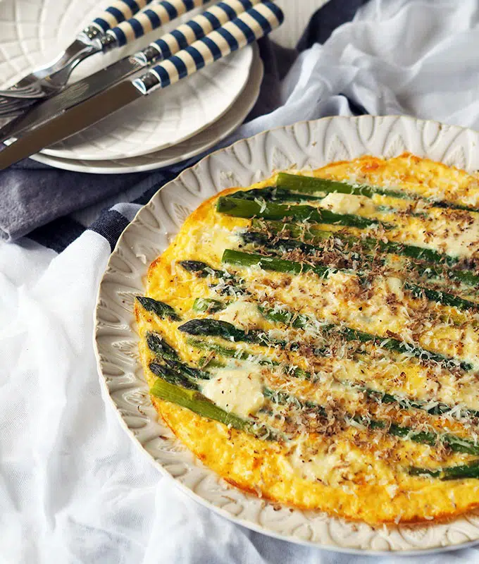 above view of asparagus frittata on a white serving plate with smaller serving plates and cutlery