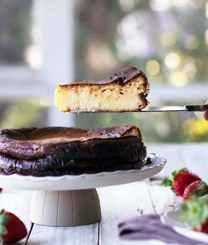 sicde view of basque burnt cheesecake on a cake stand with a slice being removed