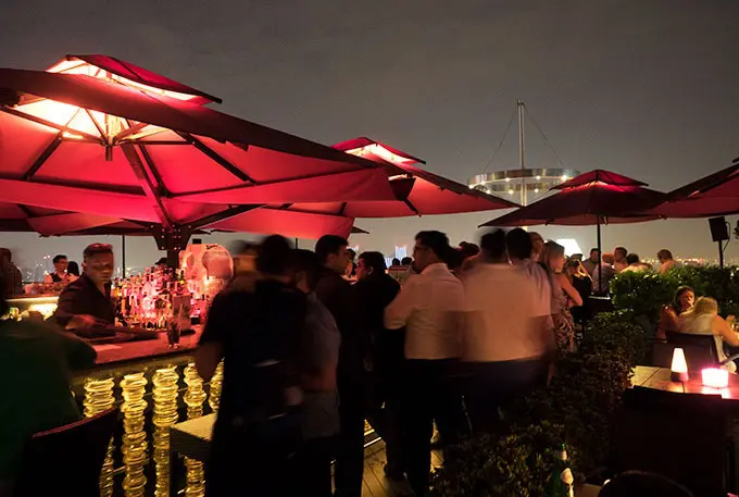 tables, chairs, people and red umbrellas at night - Ce La Vi Singapore