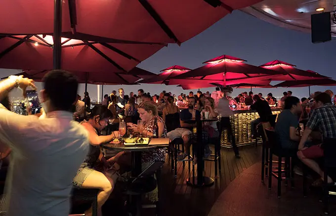 tables, chairs, people and red umbrellas at night - Ce La Vi Singapore