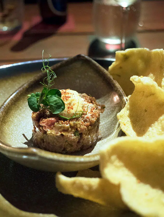 beef tartare on a small bowl topped with cream and green herb with chips on the side - Ce La Vi Singapore