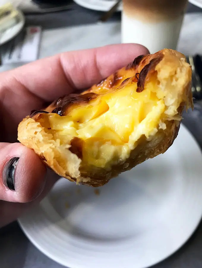 macanese egg tart being held with a bite taken out of it showing the custard