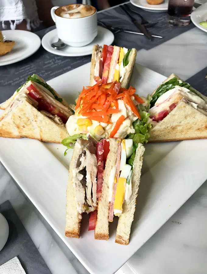 club sandwich cut into four triangle pieces on a white square plate