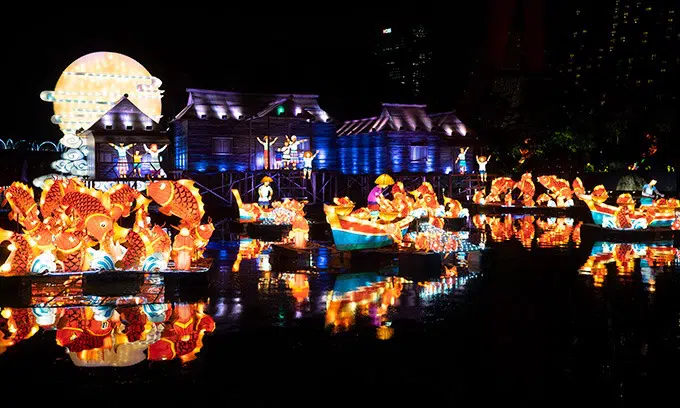 lanterns of fish, boats and houses lit up on the water