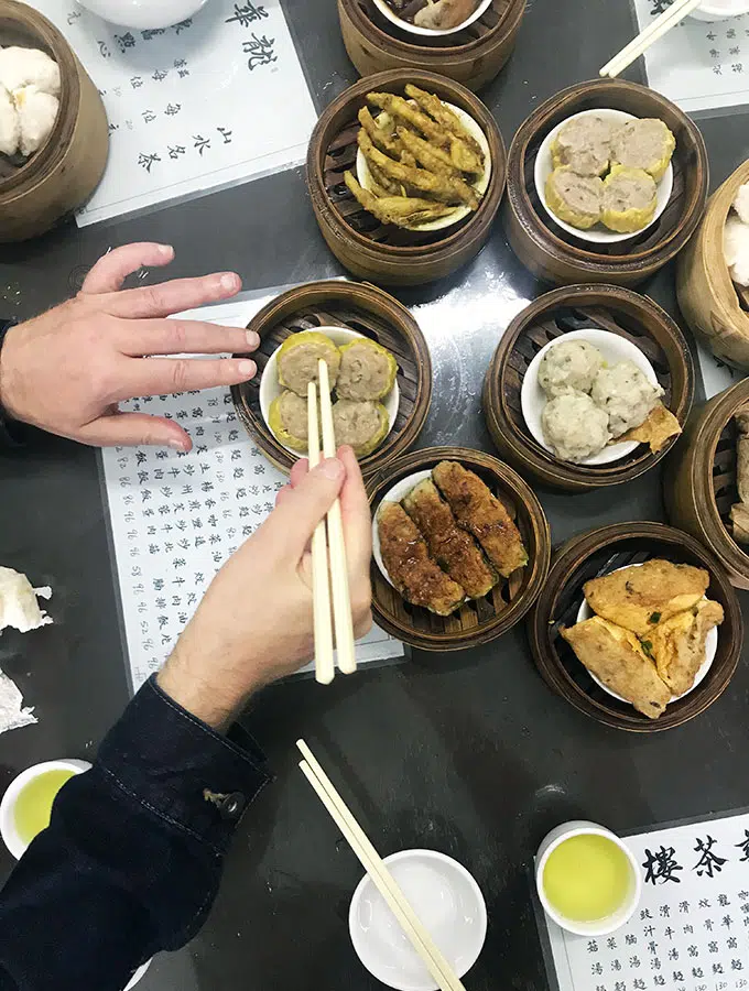 a selection of dumplings in steamer baskets on a table with a person taking one with chopsticks