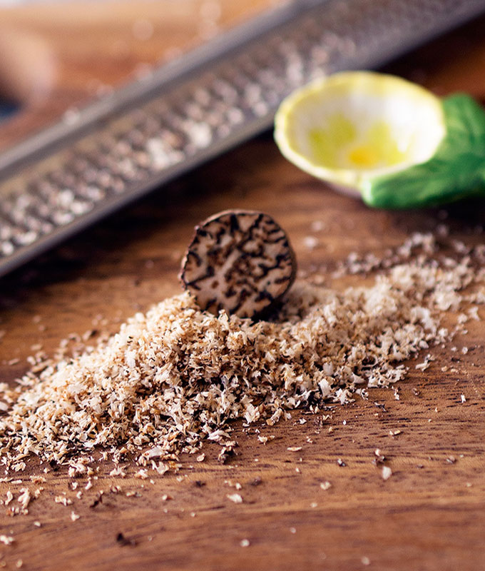 whole nutmeg sitting on a pile of ground nutmeg on a board