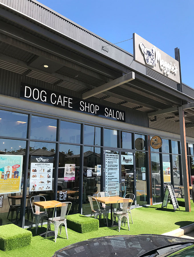 the outside facade of maggies dog cafe with out door tables and fake grass