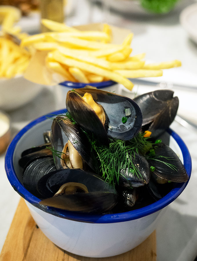 mussels in a blue rimmed bowl with fries in the back ground