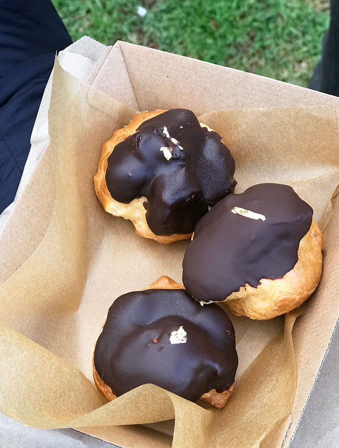 profiteroles covered in chocolate in a cardboard boxed lined with brown paper