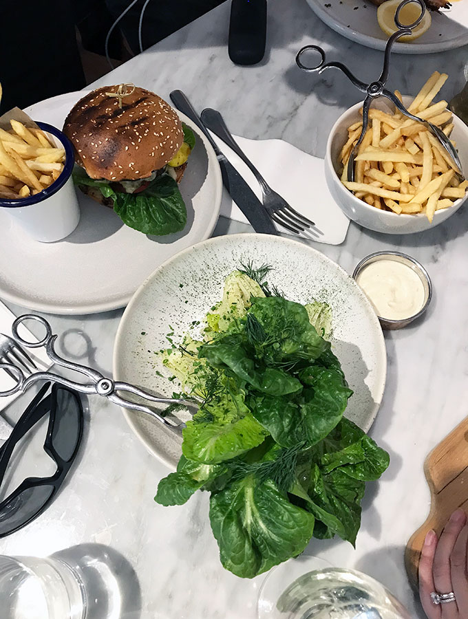 top view of dishes on the table, including a hamburger with chips, a green leaf salad, and a bowl of fries