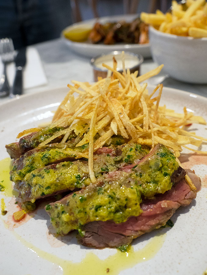 steak and french fries on a plate with french fries in a bowl in the back ground