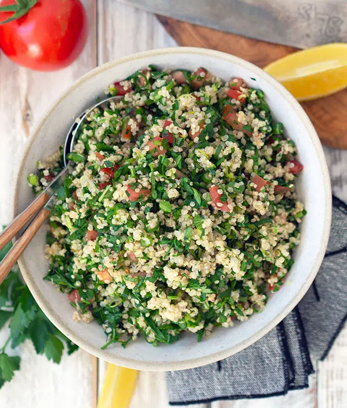 tabouli in a ceramic serving bowl on a table with wedges of lemon