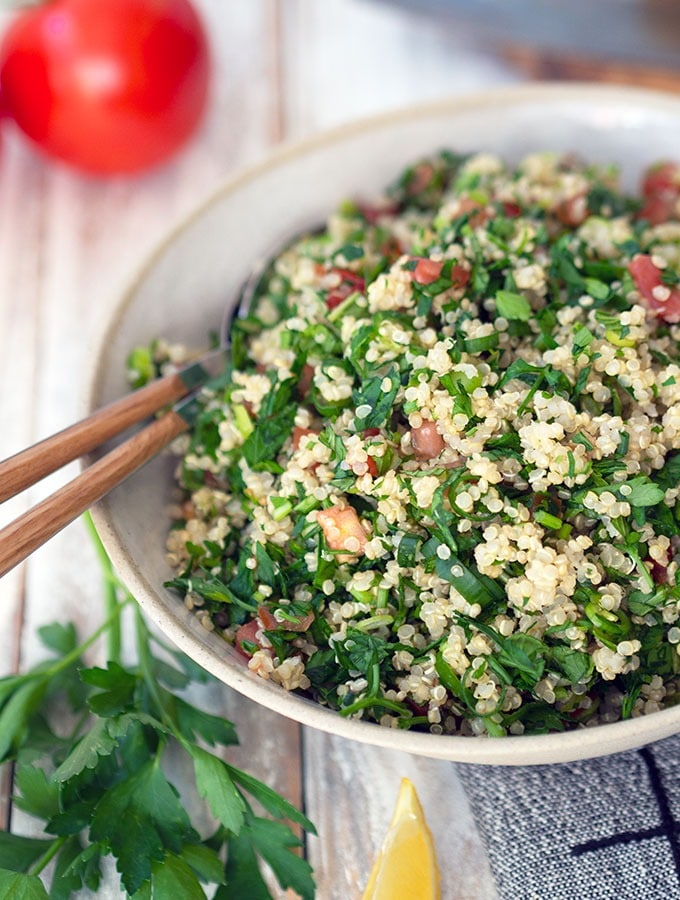 tabouli in a ceramic serving bowl on a table with wedges of lemon