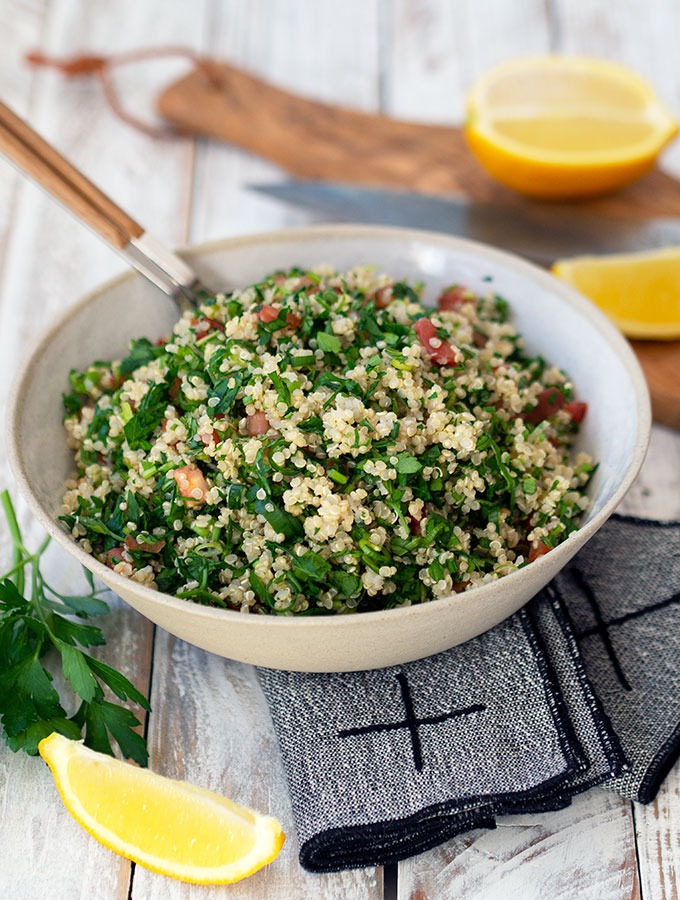 tabouli in a ceramic serving bowl on a table with wedges of lemon