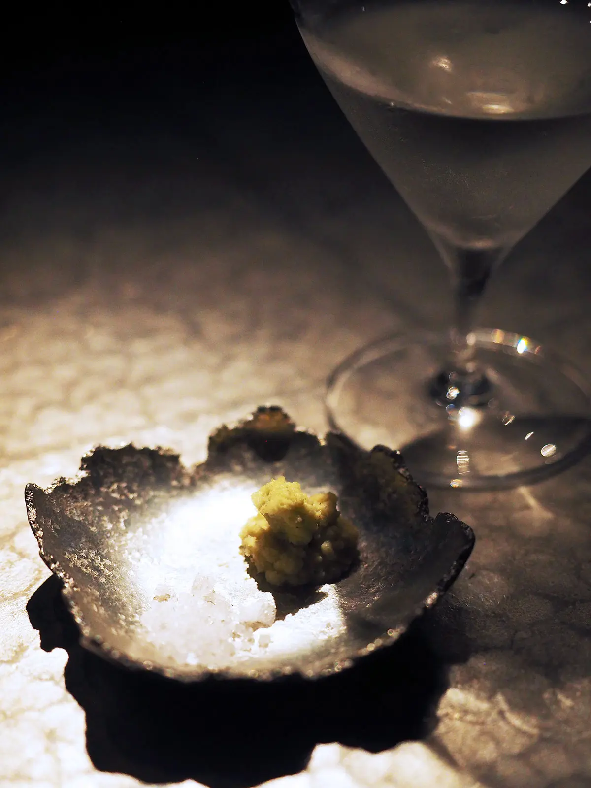 decorative silver dish with wasabi and salt sitting next to a glass