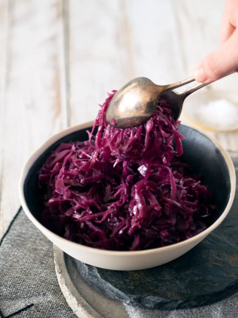 somebody holding spoons and lifting the cooked cabbage out of a bowl to serve