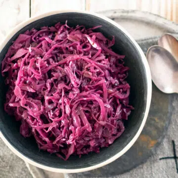 braised red cabbage in a bowl, on a plate with two spoons at the side