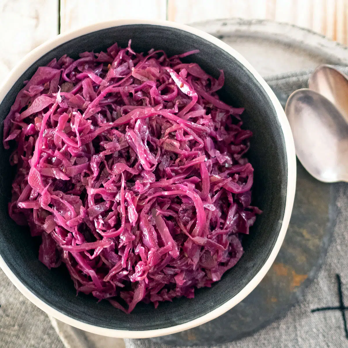 braised red cabbage in a bowl, on a plate with two spoons at the side