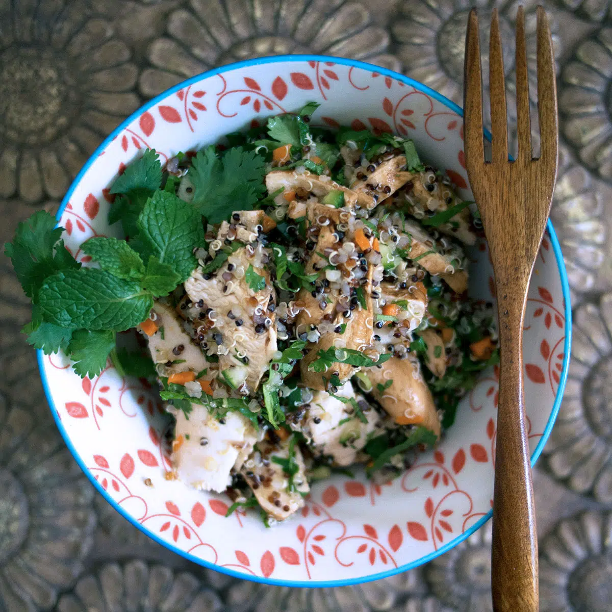 chicken quinoa salad in a round bowl with a wooden fork