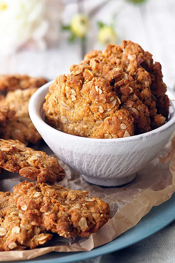 Anzac biscuits in a bowl sitting on a plate with more Anzac biscuits