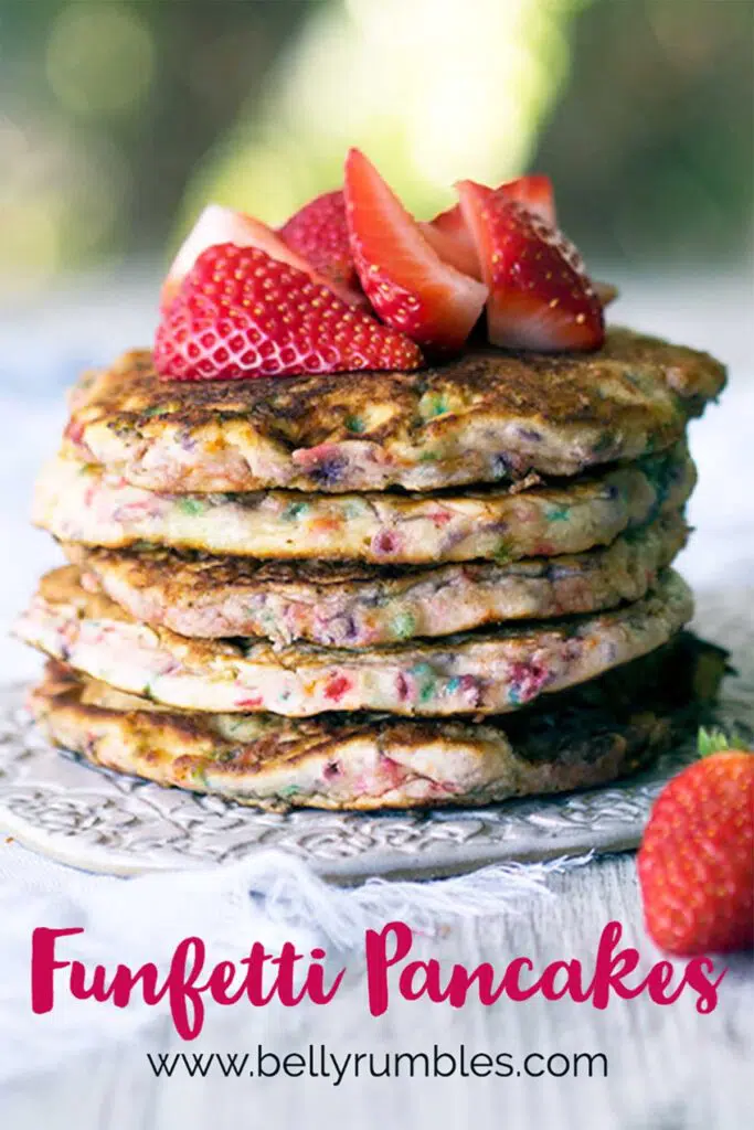 stack of funfetti pancakes topped with fresh strawberries sitting on a white plate