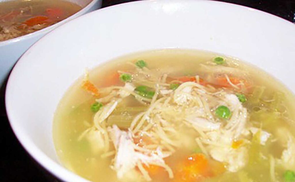 bowl of chicken soup with peas, thin noodles, carrot, chicken pieces and celery