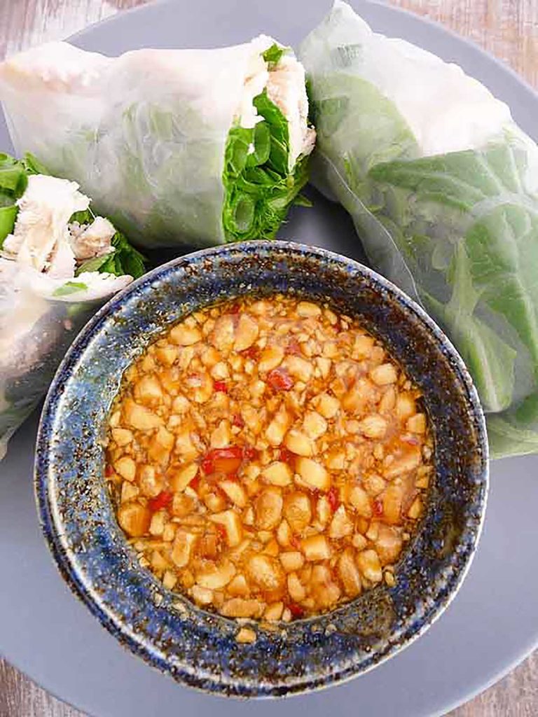 vietnamese sping roll sauce with peanuts and passion fruit in a blue bowl next to fresh spring rolls