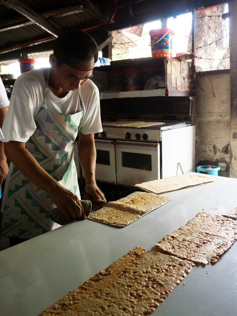 man in kitchen removing thin layers of cashew meringue from baking trays